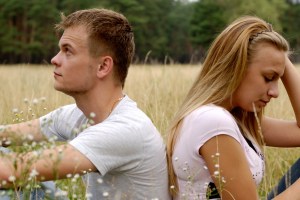 Young couple sitting on the grass back to back